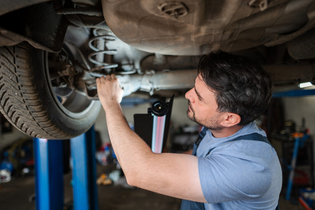 Male mechanic in blue shirt completes brake repair service on car in lift