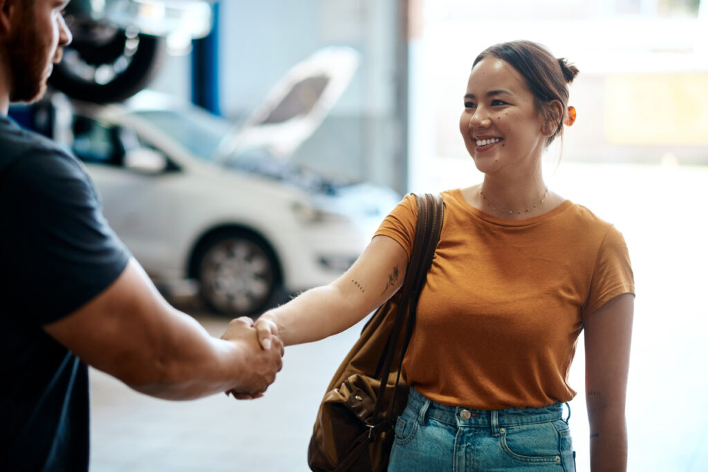 Woman in an orange top shakes mechanic's hand after booking a car service at Davey Motor Group