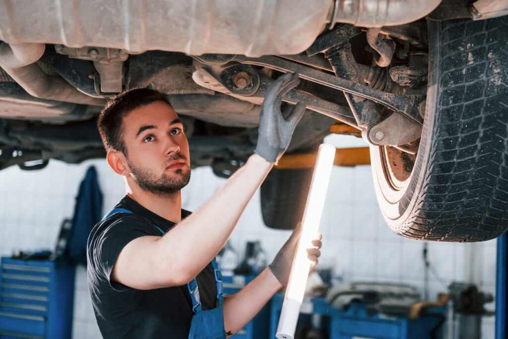 Mechanic standing under a car on a hoist doing a car suspension service while wearing grey gloves